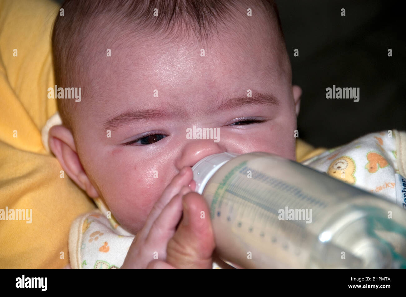 Un an closeup portrait bébé fille des boissons du biberon en plastique avec la main de la mère d'aider Banque D'Images