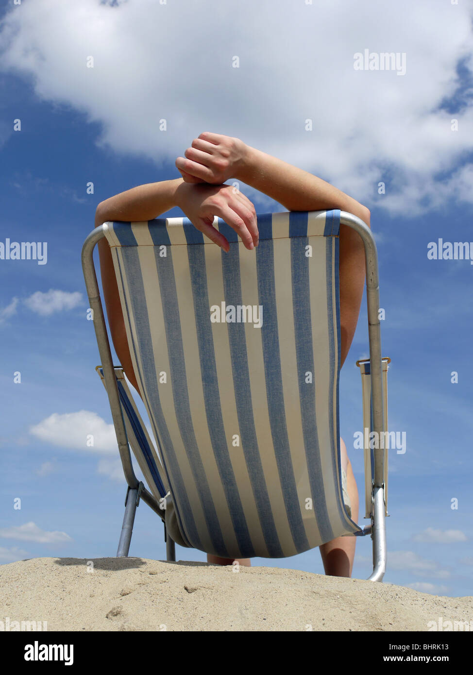 Femme en train de bronzer sur une chaise longue sur la plage tourné contre le ciel bleu Banque D'Images