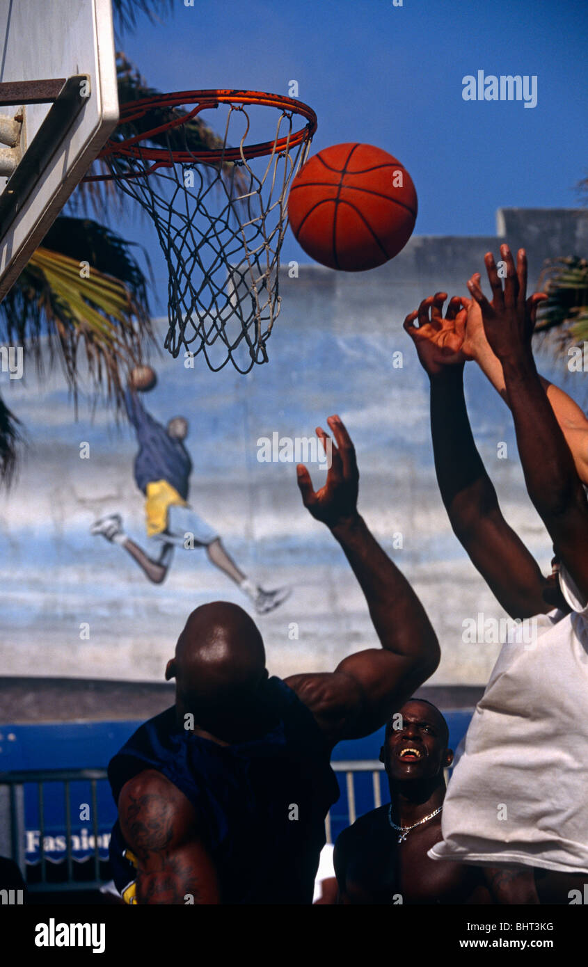 Trois jeunes hommes afro-américains à sauter haut pour un terrain de basket-ball avec est un quatrième bras essayant de faire contact avec la balle Banque D'Images