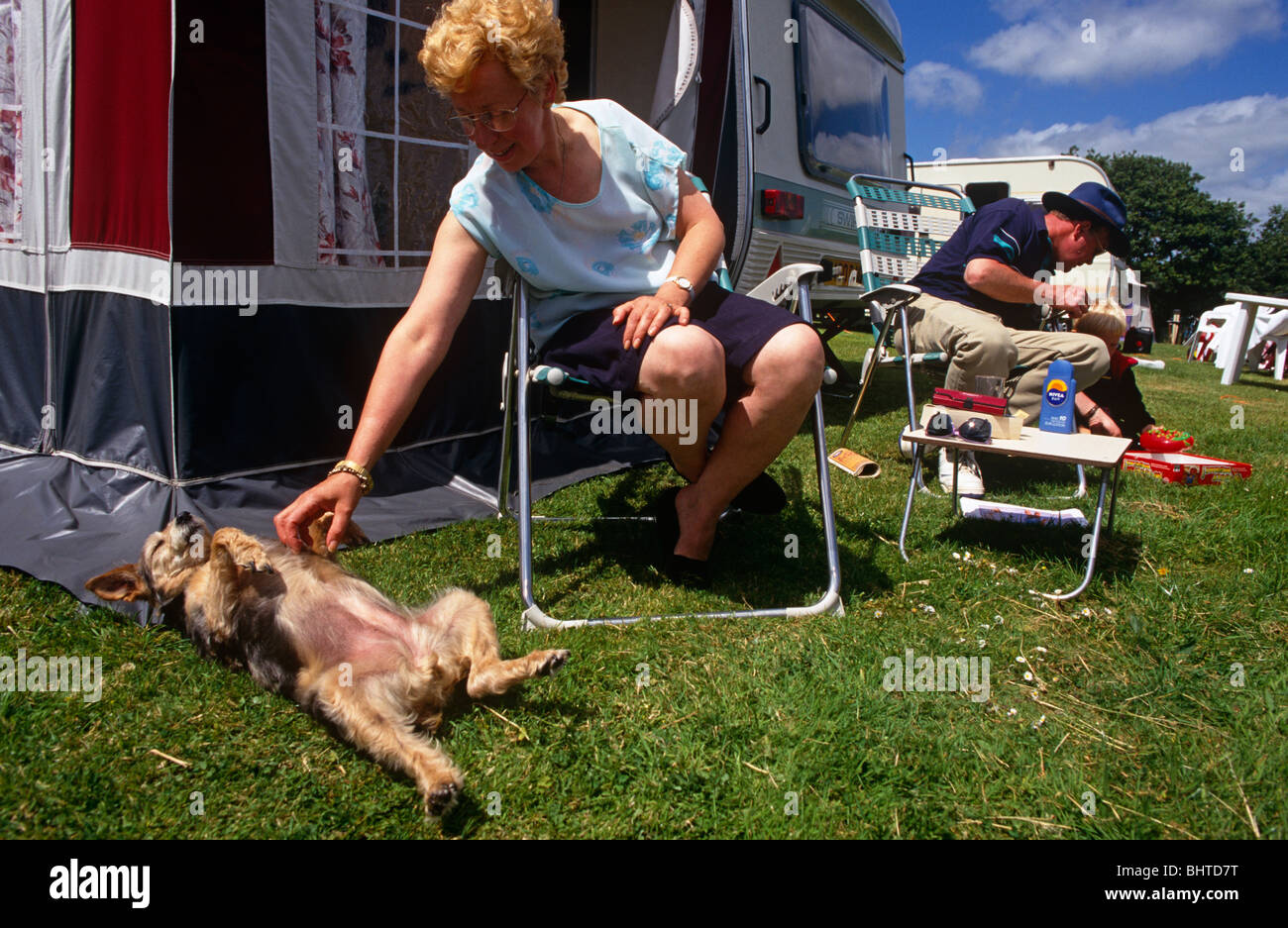 Un mari, femme, enfant et son chien sont caravan campeurs qui sont de détente dans des chaises à l'extérieur de leur caravane's store. Banque D'Images
