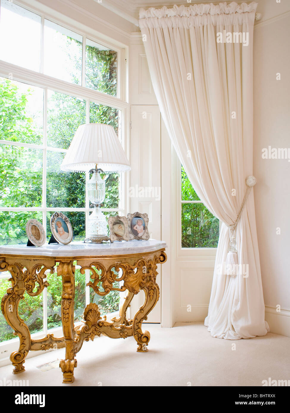 Recouvert de marbre antique gilt table console en baie vitrée avec rideaux crème Banque D'Images