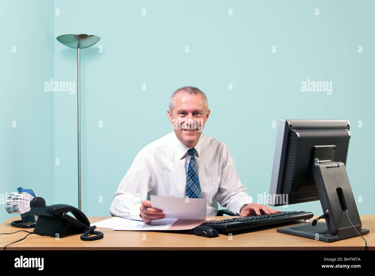 Un homme d'âge mûr s'assit à son bureau, regardant vers la caméra et sourit. Banque D'Images