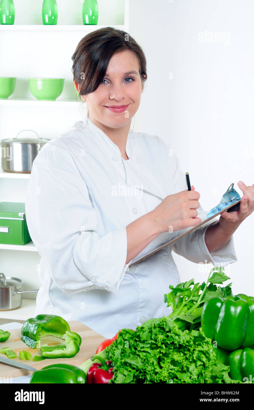 Femme Chef Making Notes sur un presse-papiers dans sa cuisine Banque D'Images