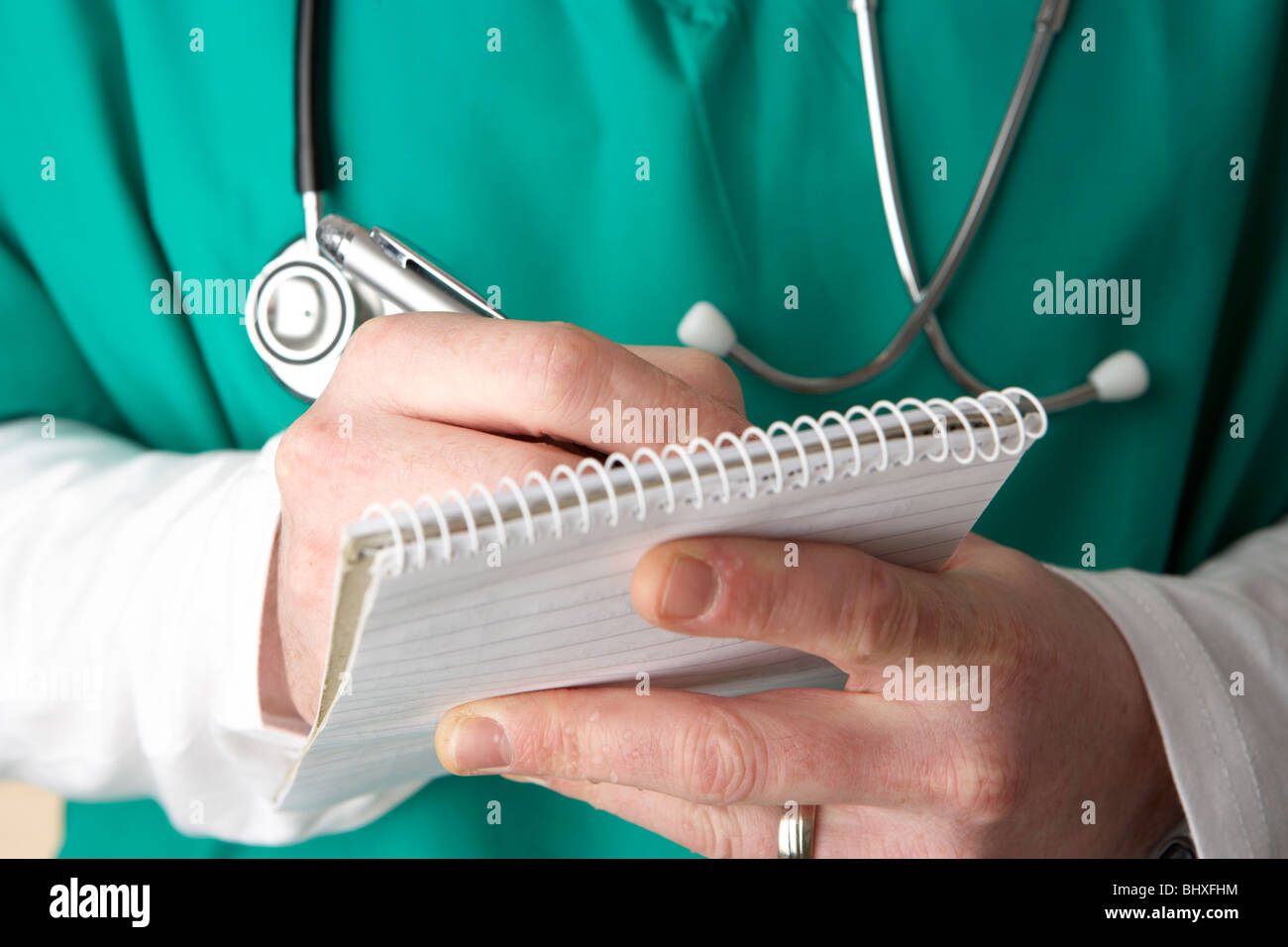 Man wearing scrubs medical stéthoscope et à écrire des notes sur un ordinateur portable Banque D'Images