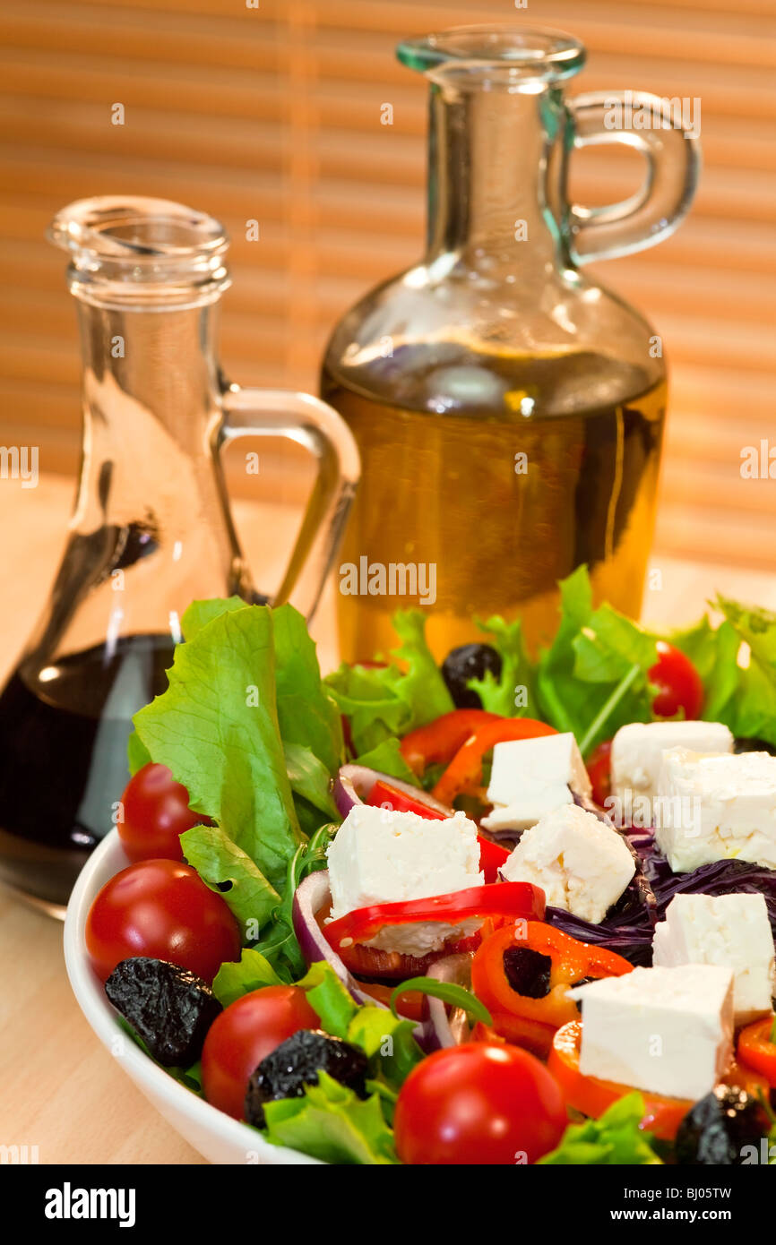 Salade, tomate, poivron rouge, oignon rouge, olive noire et le fromage feta salade avec bouteilles d'huile d'olive et vinaigre balsamique Banque D'Images