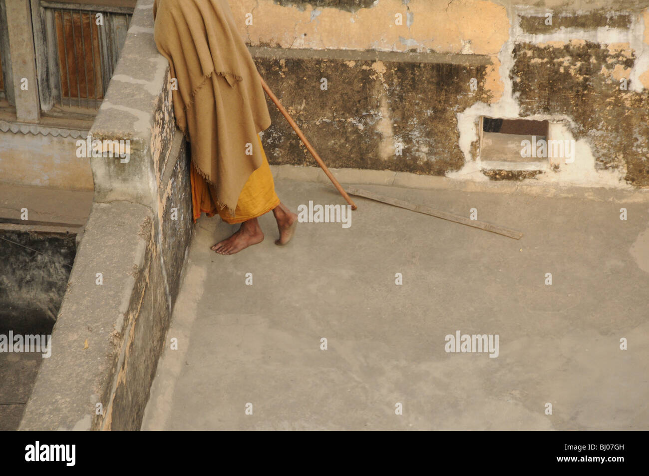 Un homme sans chaussures sur se tient sur son toit avec un bâton pour repousser loin des singes dans Varanasi, Inde Banque D'Images