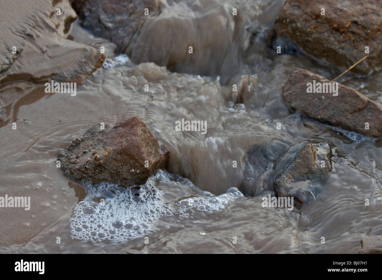 L'eau de mer sur les rochers, tumbling sur du sable comme marée basse Banque D'Images