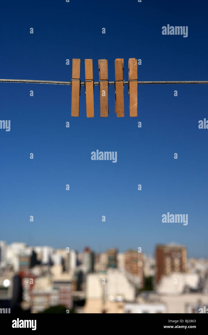 Cinq clothespegs close up accroché à un lave-ligne avec ciel bleu au-dessus des toits Banque D'Images