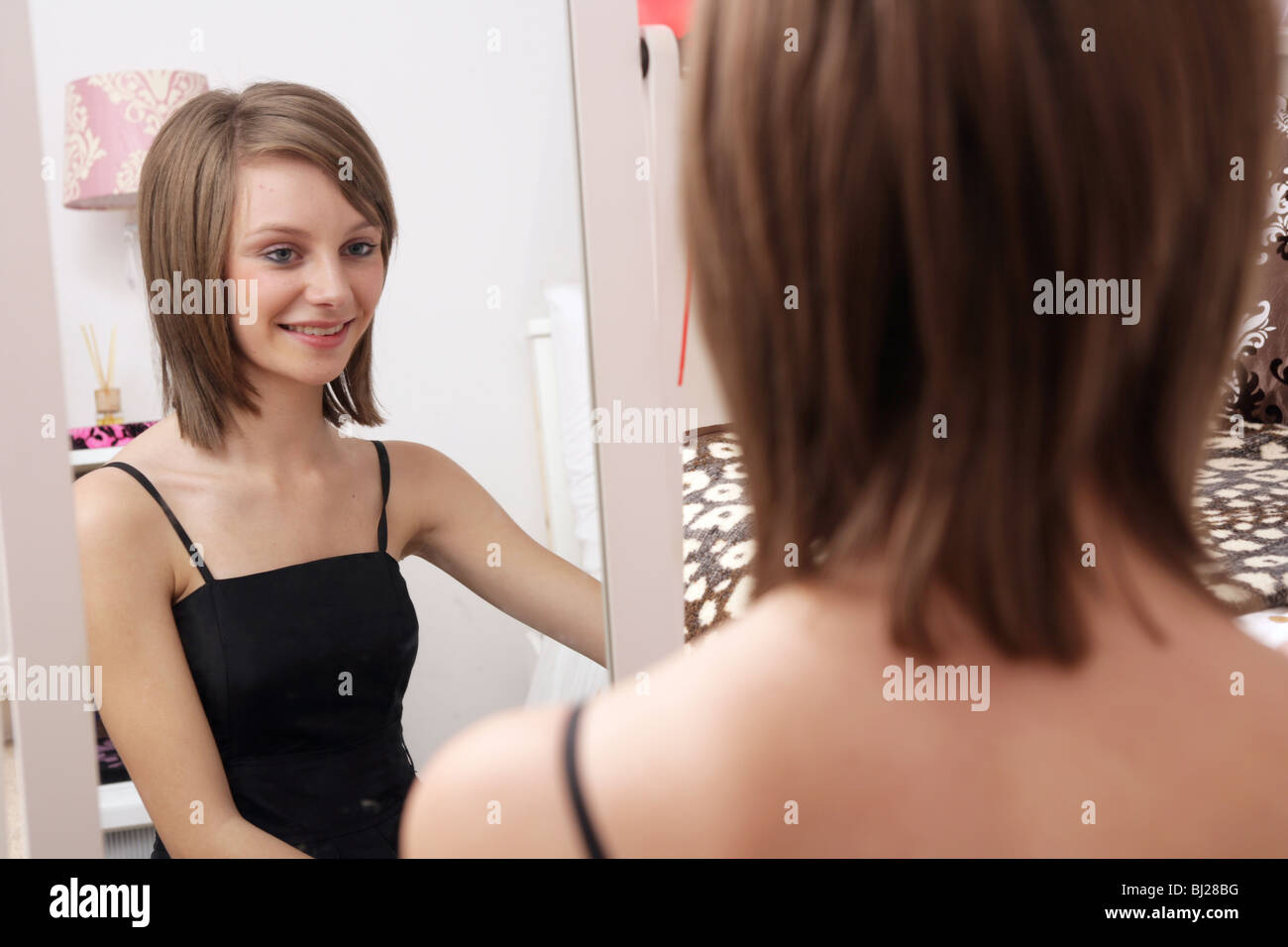 Jeune fille de 14 ans, assis sur son lit à la recherche d'elle-même dans sa chambre, miroir. Banque D'Images