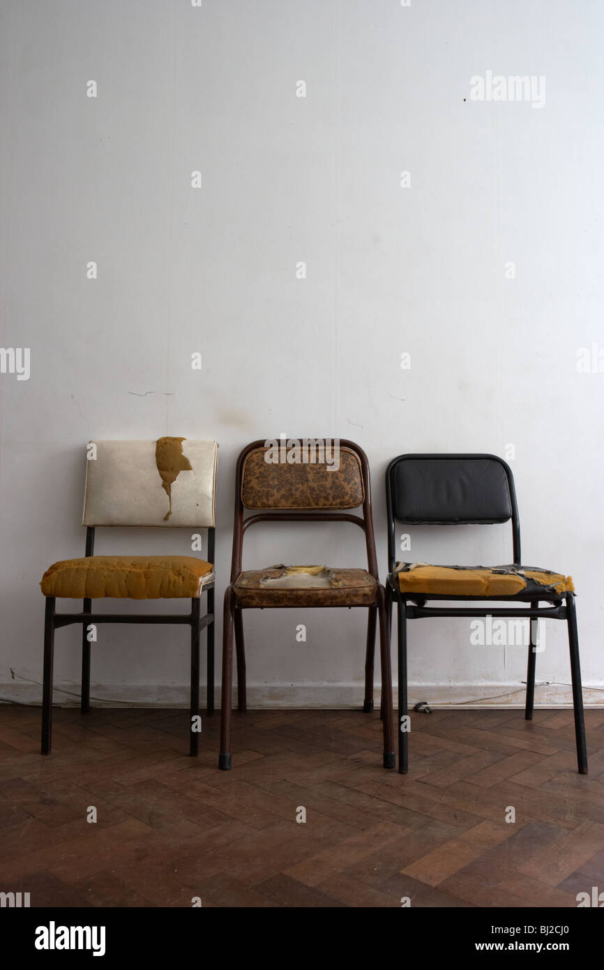 3 anciennes chaises sales usé contre un mur blanc dans un appartement délabré en Argentine Banque D'Images