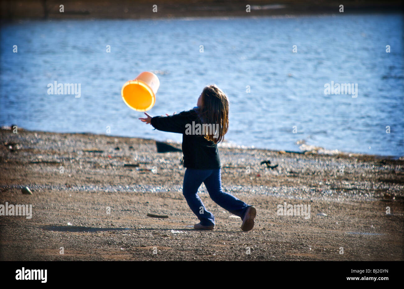 Fille jouant avec un seau par l'eau Banque D'Images