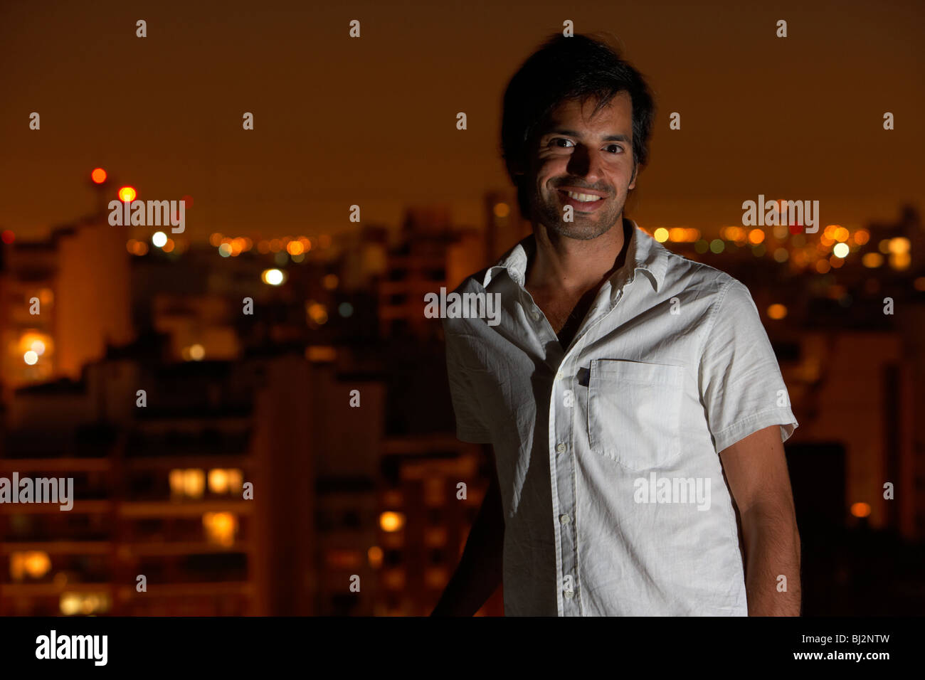 L'Amérique latine hispanique homme debout sur la terrasse du toit souriant de soir à l'arrière-plan de la ville de Buenos Aires Argentine Banque D'Images