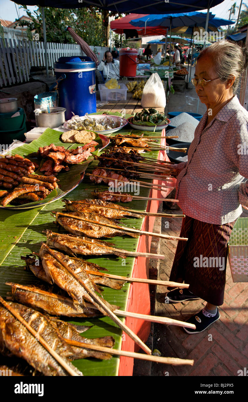 Une vieille femme Lao choisir du poisson grillé dans le marché de Luang Prabang au Laos Banque D'Images