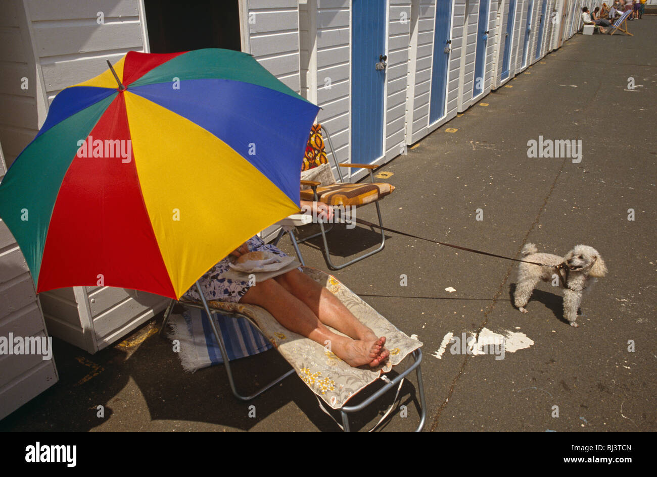 Une dame protège elle-même d'un milieu de journée d'été d'été avec un soleil parasol brolley de couleur vive. Banque D'Images