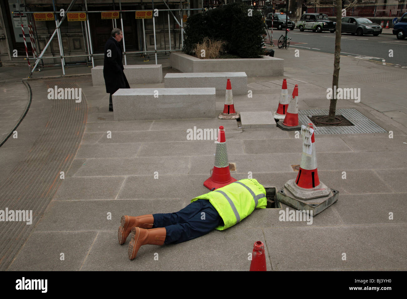 Un ouvrier d'entretien de la route se trouve sur le sol avec sa tête dans un trou Banque D'Images