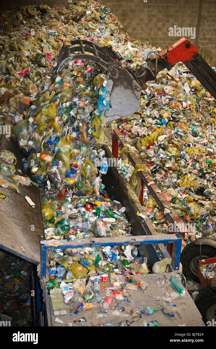 Centre de tri des déchets recyclables. Un chargeur télescopique déverse un seau de déchets plastiques sur la chaîne de tri sélectif. Banque D'Images