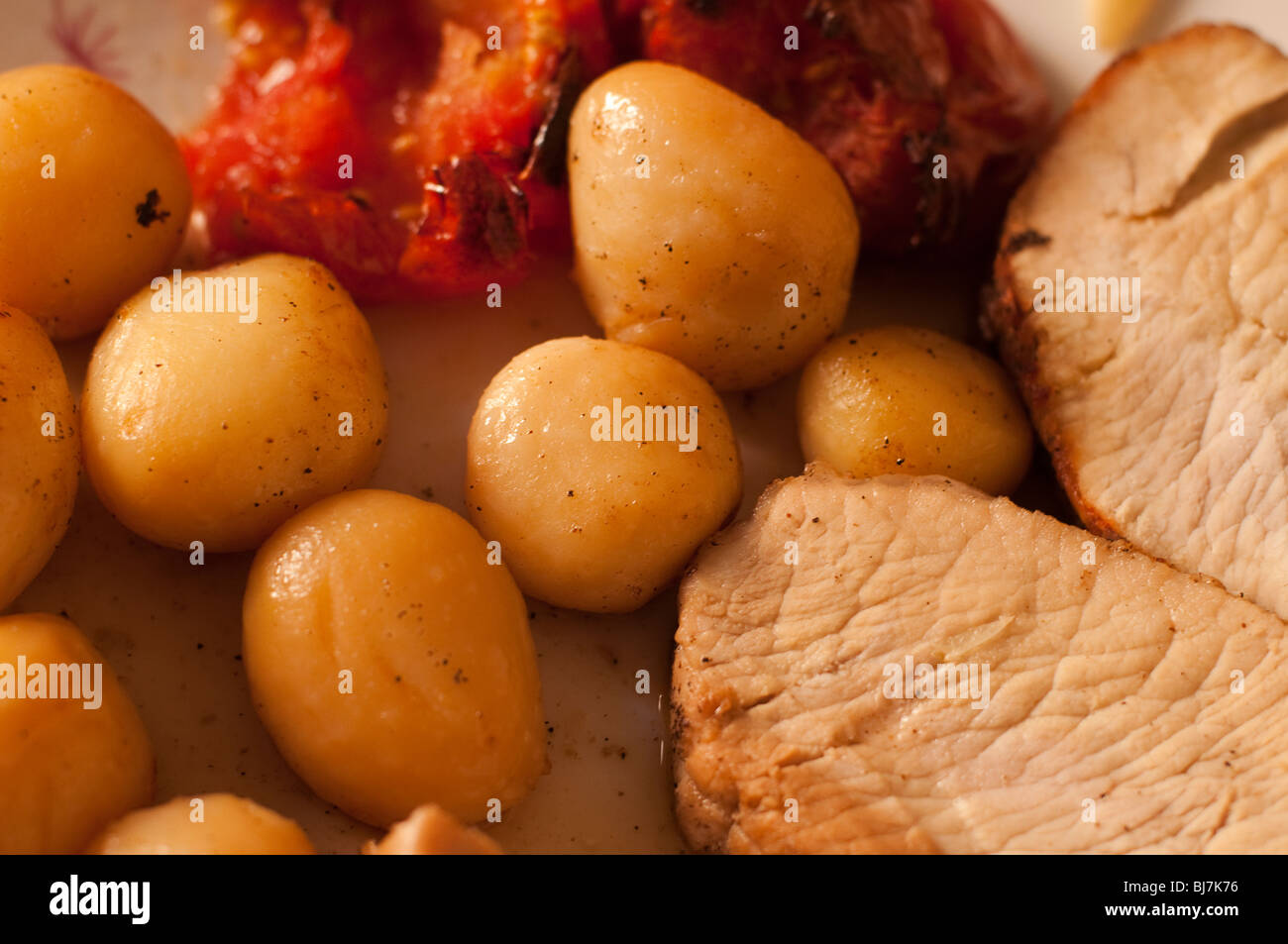 Petit tour des pommes de terre et les tomates avec des tranches de porc dans une assiette blanche, cuits au four Banque D'Images