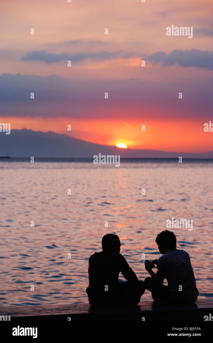 Silhouette de couple sitting on wall au coucher du soleil sur la baie de Manille, de Manille, Philippines Banque D'Images
