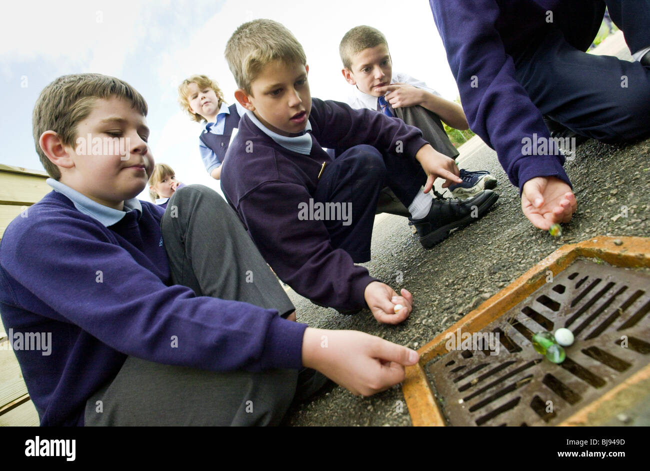 Garçons jouant aux billes d'une aire de jeux traditionnels se joue sur la cour de récréation d'une école au Pays de Galles, Royaume-Uni Banque D'Images