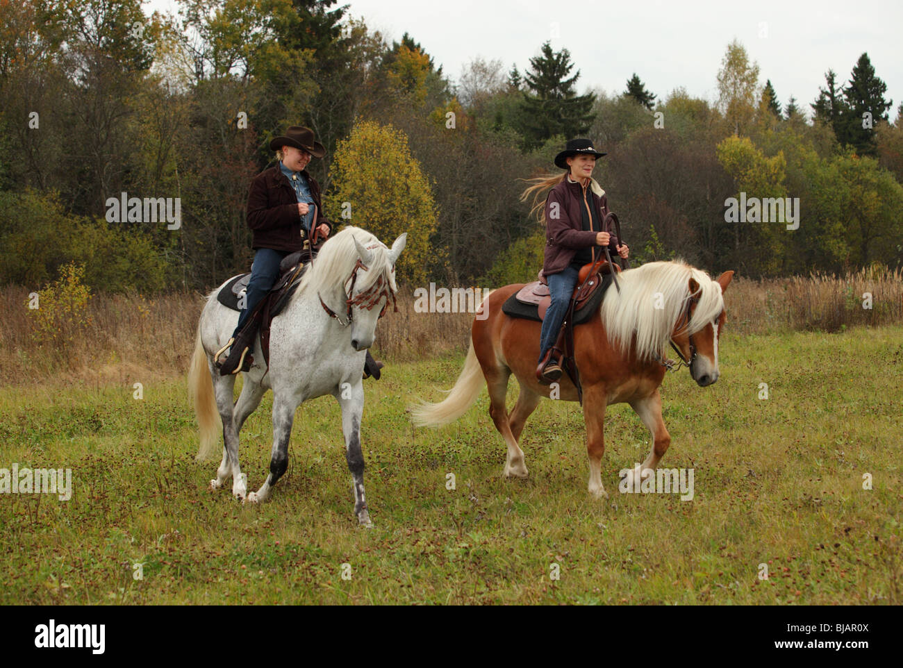 Deux femmes vêtues de vêtements et les chapeaux de cowboy de l'équitation western à cheval dans un ranch Banque D'Images