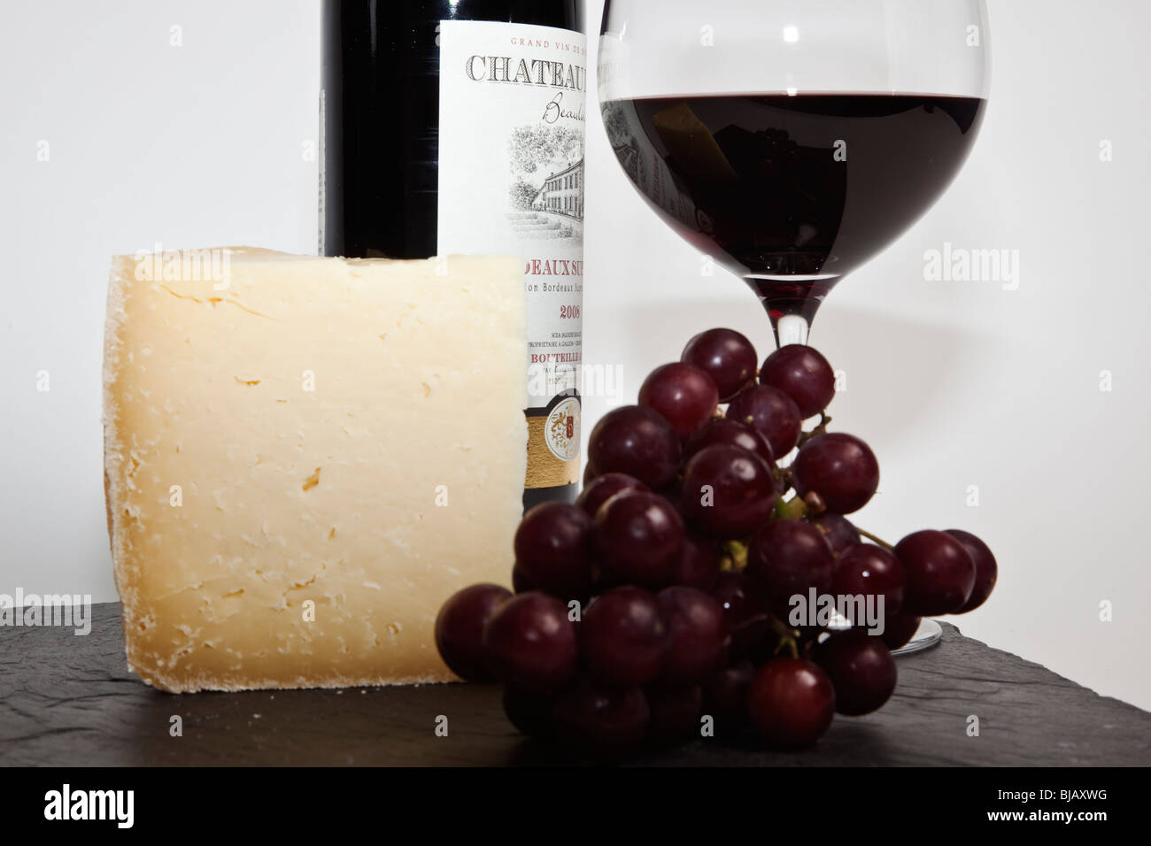 Still Life de vin rouge, un morceau de fromage, raisins et une bouteille de vin rouge sur une ardoise noire sur un fond blanc Banque D'Images