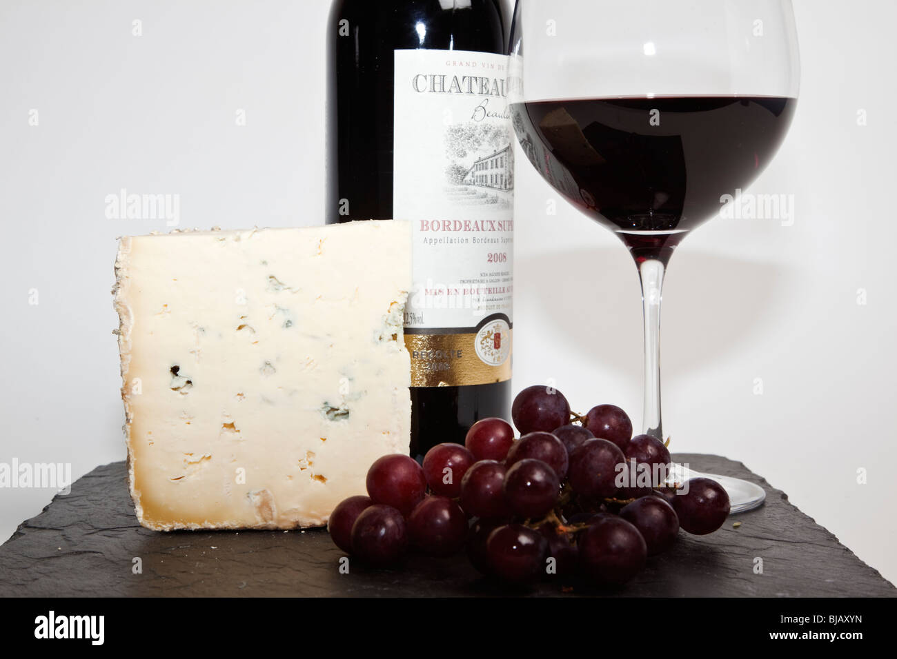 Still Life de vin rouge, un morceau de fromage bleu, raisin et une bouteille de vin rouge à l'ardoise noire sur un fond blanc Banque D'Images