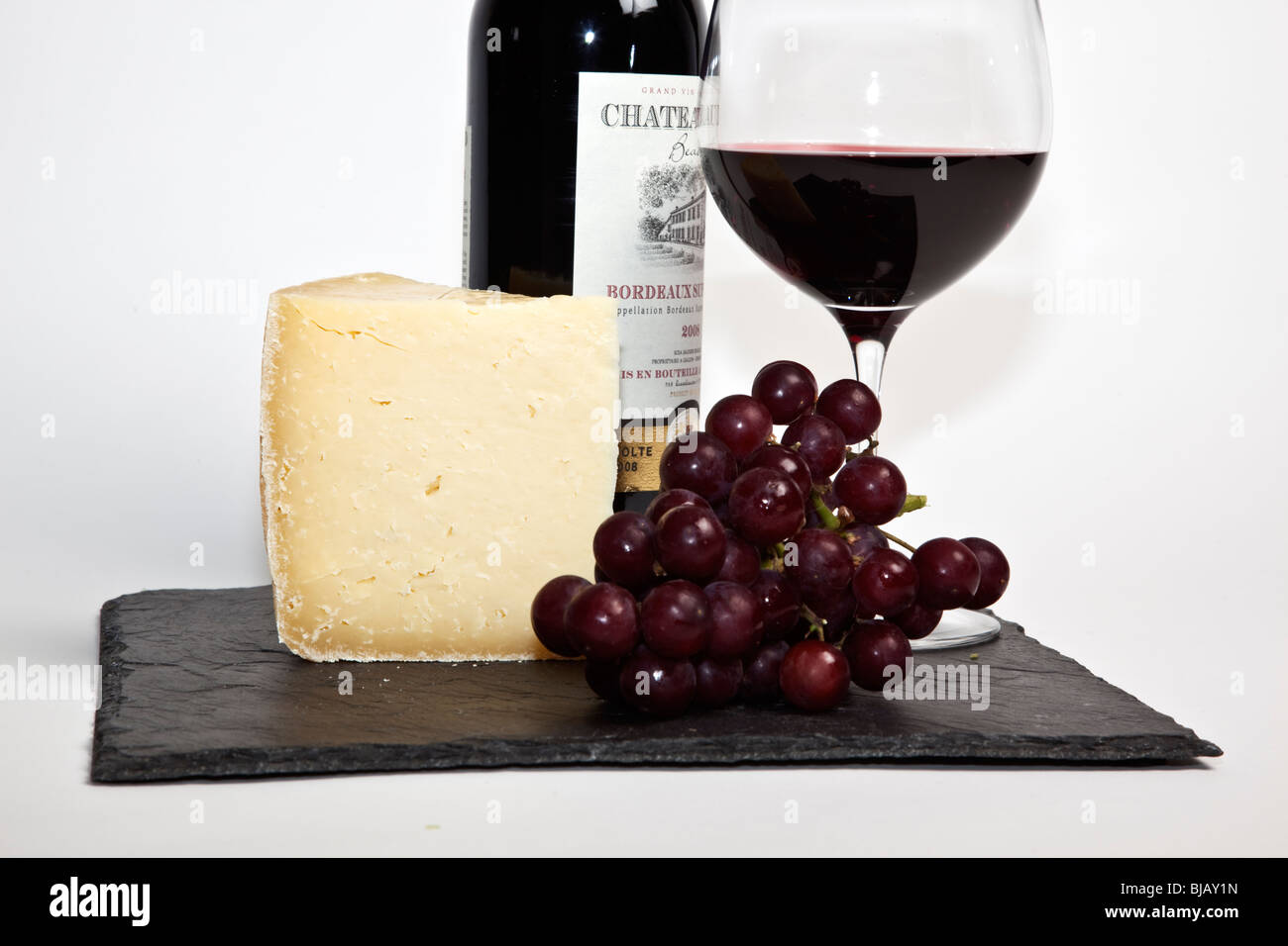 Still Life de vin rouge, un morceau de fromage, raisins et une bouteille de vin rouge sur une ardoise noire sur un fond blanc Banque D'Images