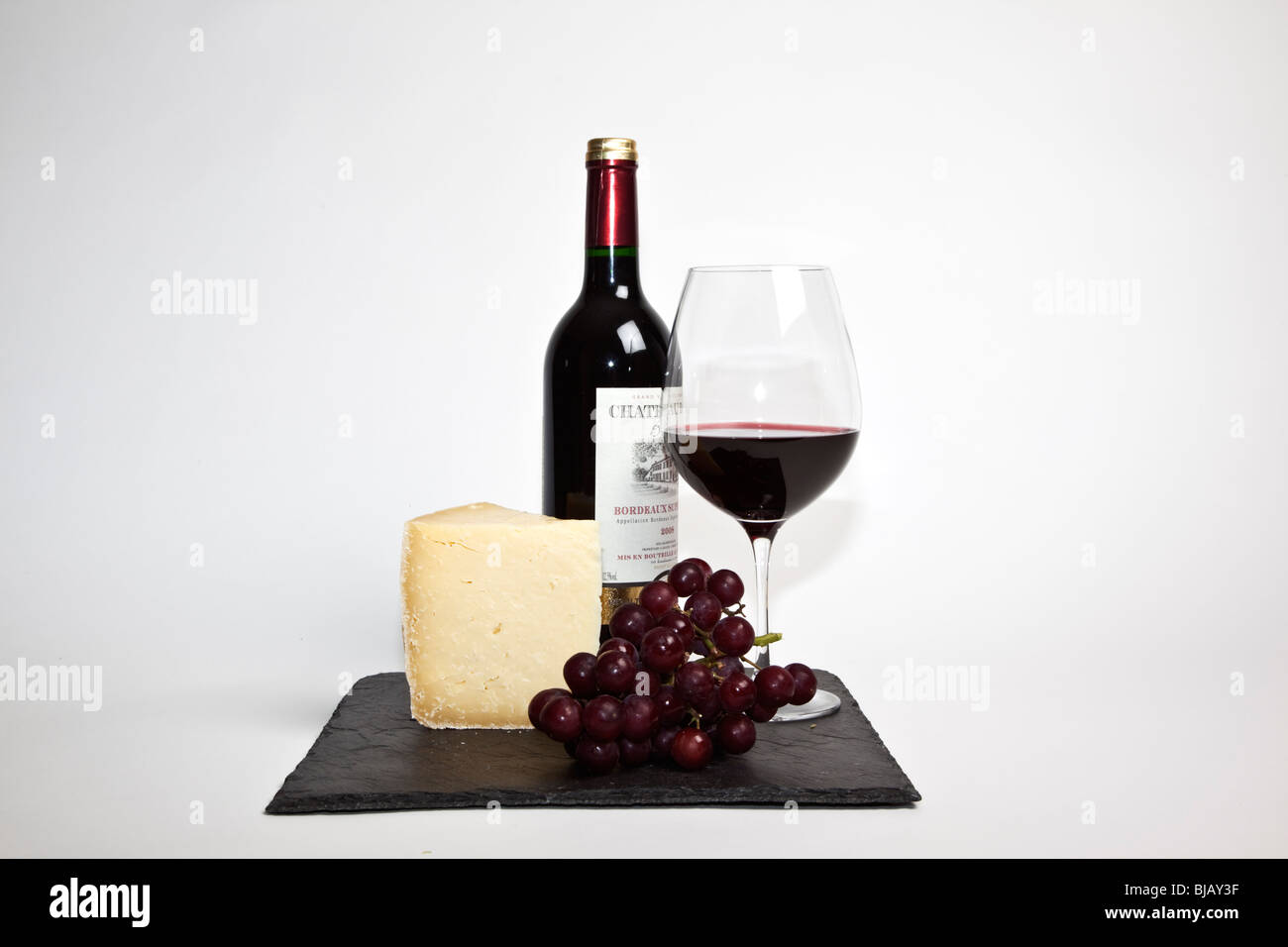Still Life de vin rouge, un morceau de fromage, raisins et une bouteille de vin rouge sur une ardoise noire sur un fond blanc Banque D'Images