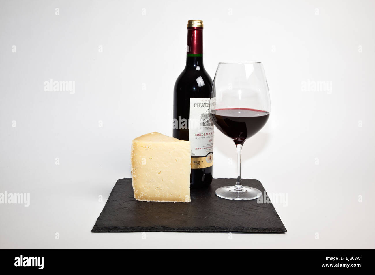 La vie encore d'un verre de vin rouge, un morceau de fromage et une bouteille de vin rouge sur une ardoise noire sur un fond blanc Banque D'Images