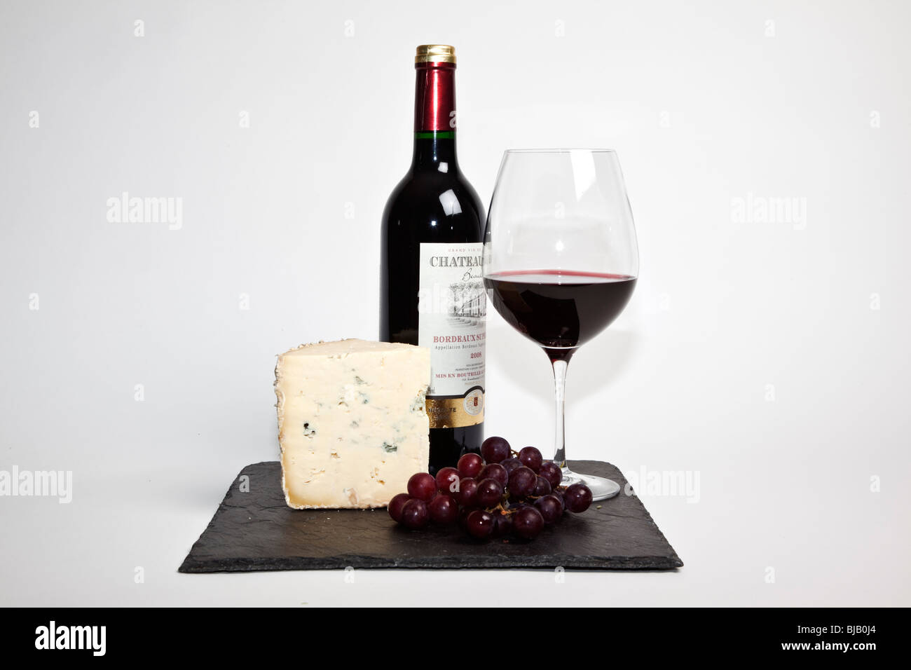 Still Life de vin rouge, un morceau de fromage, raisins et une bouteille de vin rouge sur une ardoise noire sur un fond blanc Banque D'Images