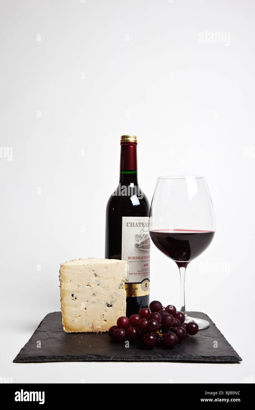 Still Life de vin rouge, un morceau de fromage bleu, raisin et une bouteille de vin rouge à l'ardoise noire sur un fond blanc backgrounde Banque D'Images