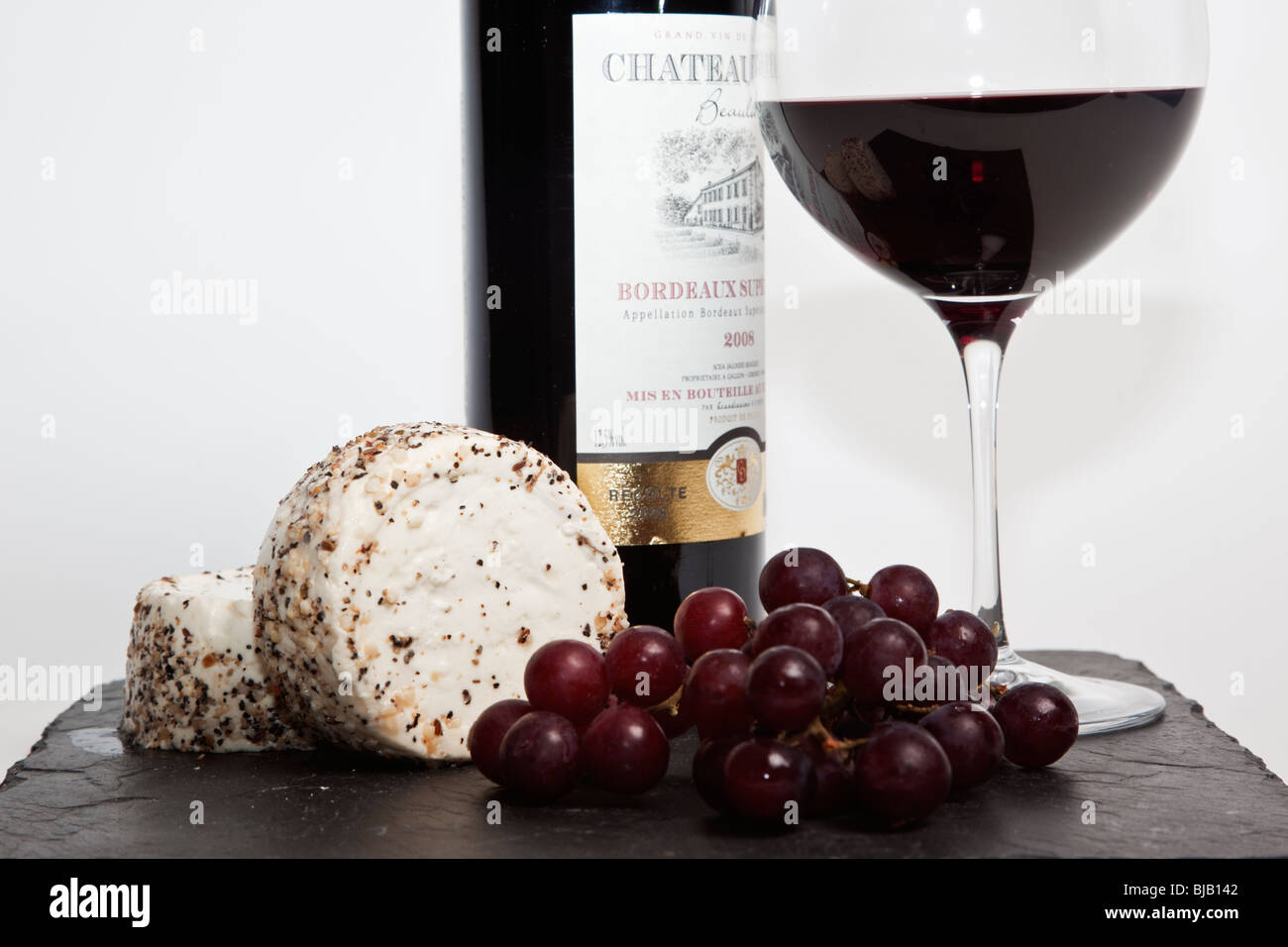 Still Life de vin rouge, un morceau de fromage à l'ail et le poivre, des raisins et une bouteille de vin rouge avec un arrière-plan uni, blanc Banque D'Images