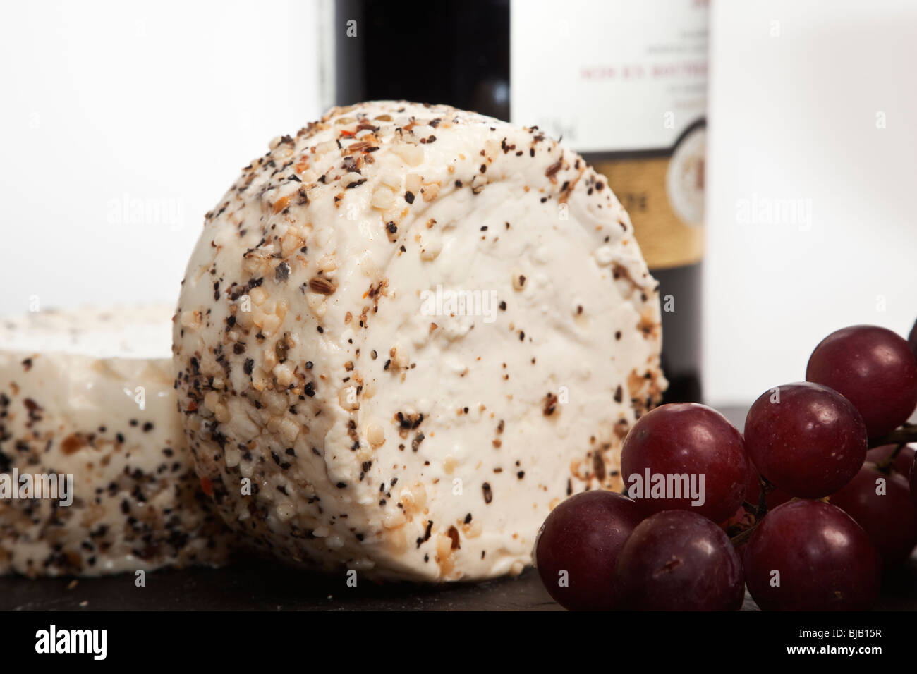 Still Life de vin rouge, un morceau de fromage à l'ail et le poivre, des raisins et une bouteille de vin rouge avec un arrière-plan uni, blanc Banque D'Images