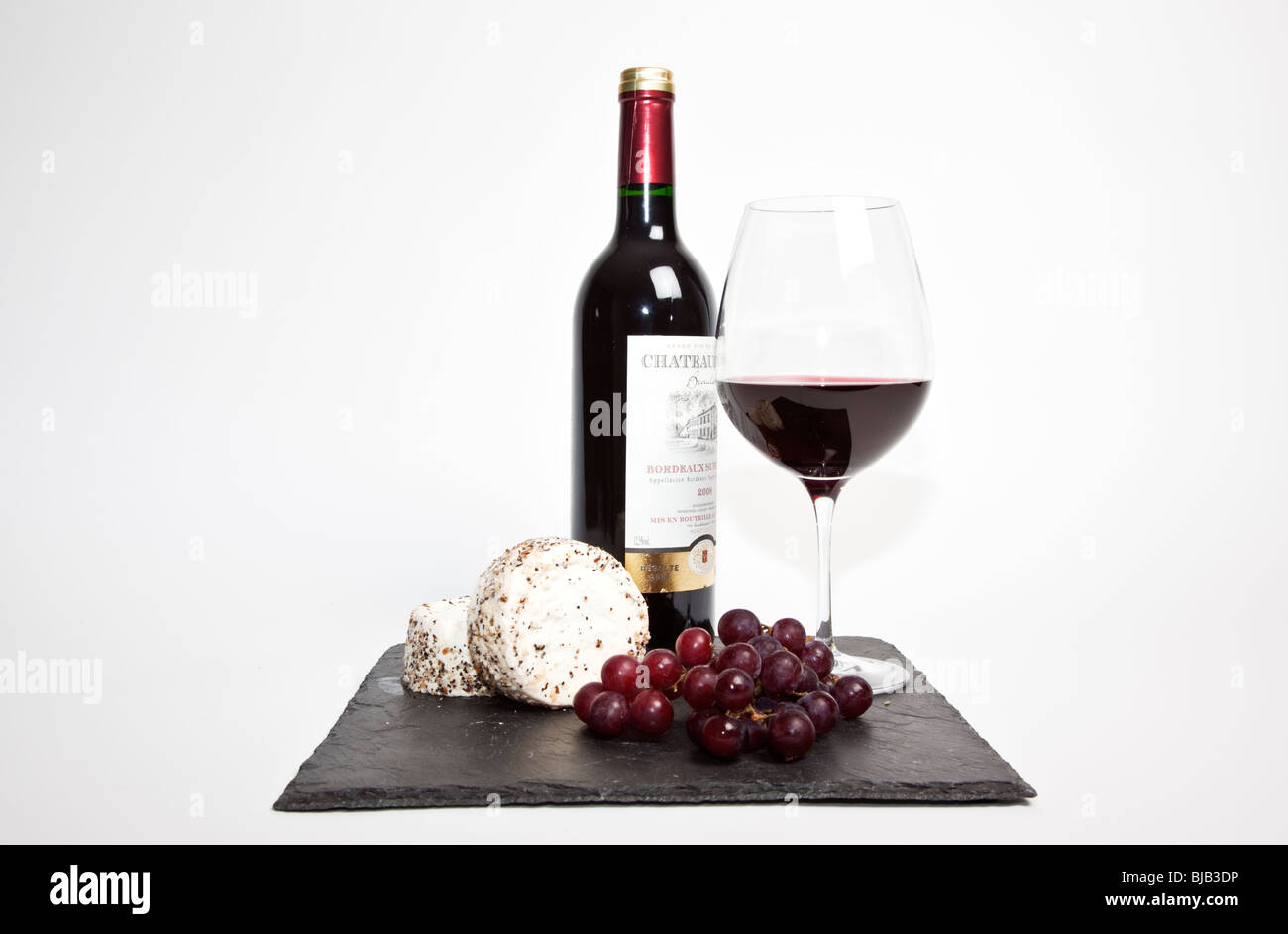 Still Life de vin rouge, un morceau de fromage bleu, raisin et une bouteille de vin rouge à l'ardoise noire sur un fond blanc Banque D'Images