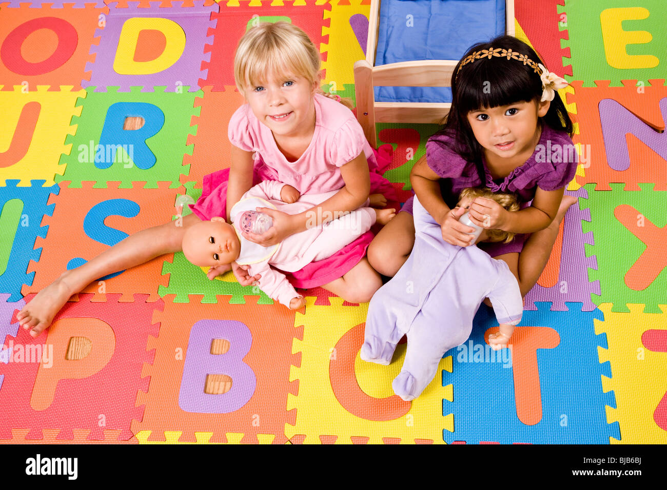 Peu de filles d'âge préscolaire jouer à la poupée sur l'alphabet coloré mat Banque D'Images