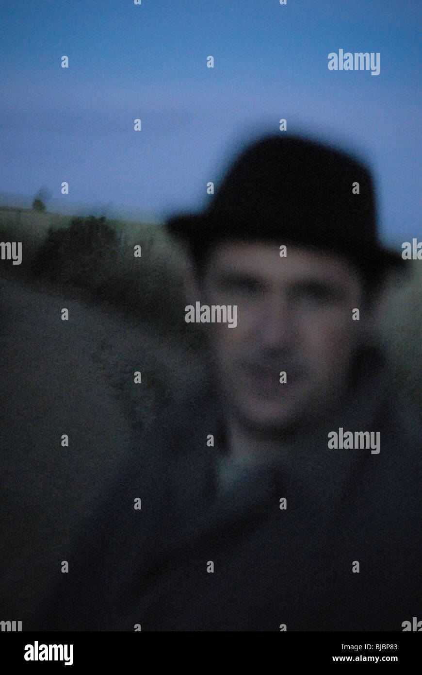 Image floue d'un homme sur le chemin de campagne dans la nuit le port d'un ranicoat et hat. Banque D'Images