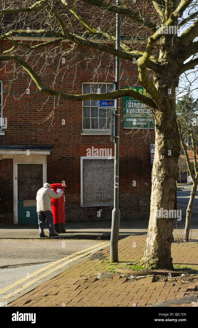 Vieux monsieur poster une lettre en un rouge traditionnel post box Banque D'Images