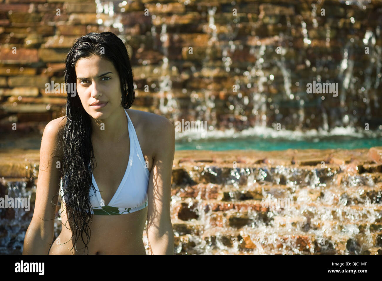 Young woman in bikini relaxing by waterfall Banque D'Images