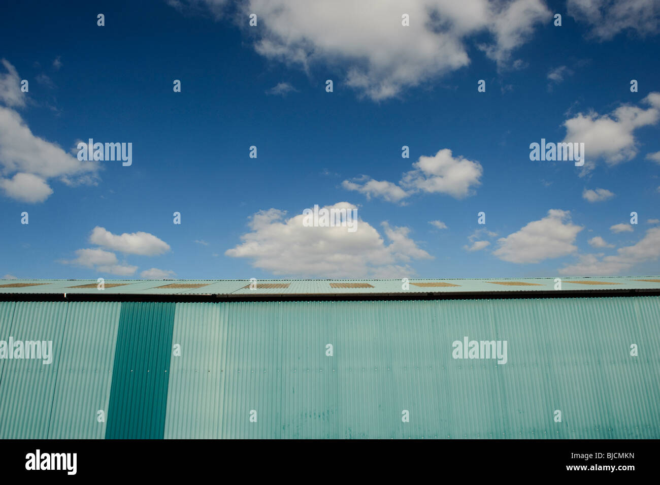 Hangar en tôle ondulée peinte en bleu, avec ciel bleu et nuages blancs Banque D'Images