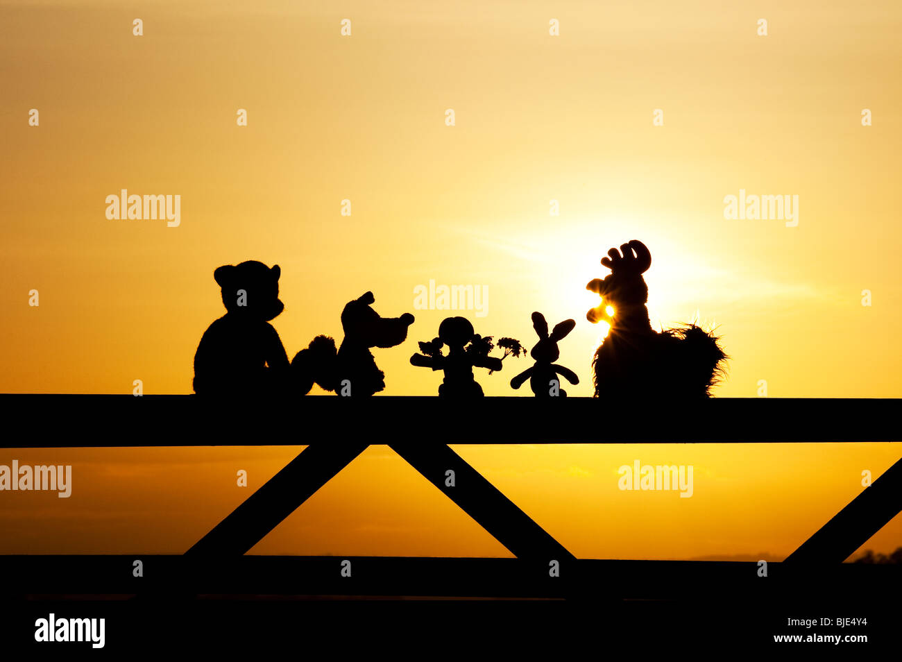 Poupée de chiffon, poulet, lapin, renard et l'ours peluches assis sur une barrière au coucher du soleil dans la campagne anglaise. Silhouette Banque D'Images