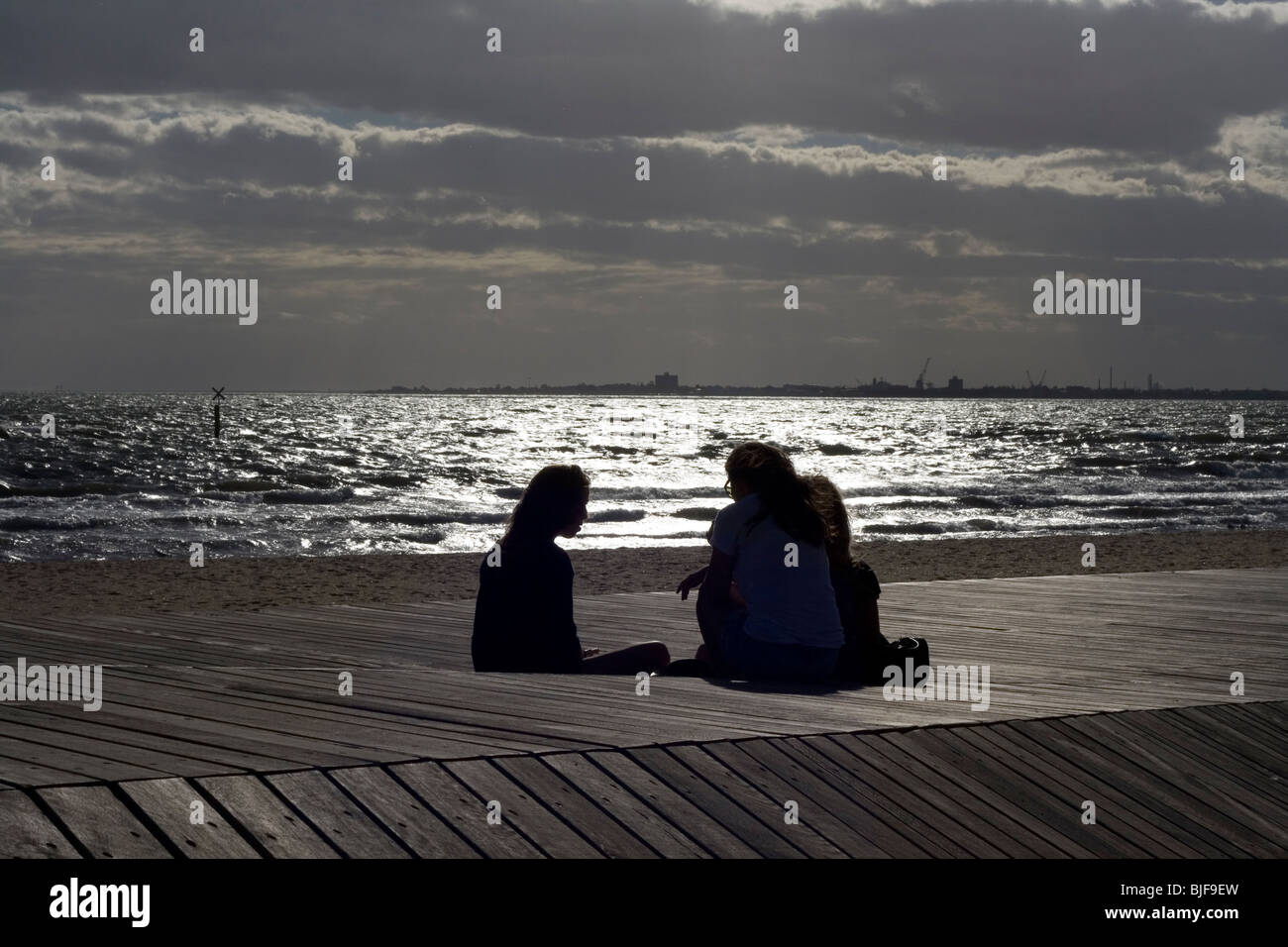 Trois amis s'asseoir sur la plage à St Kilda, Melbourne, Australie. Banque D'Images
