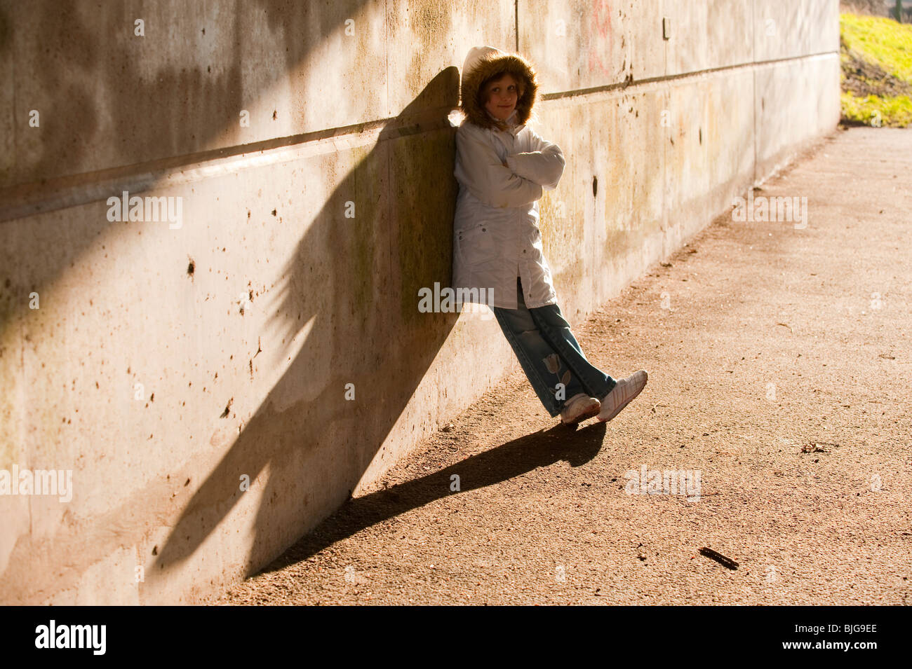 7 ans, fille en manteau d'hiver avec capuche contre mur avec de grandes ombres. Modèle entièrement libéré Banque D'Images