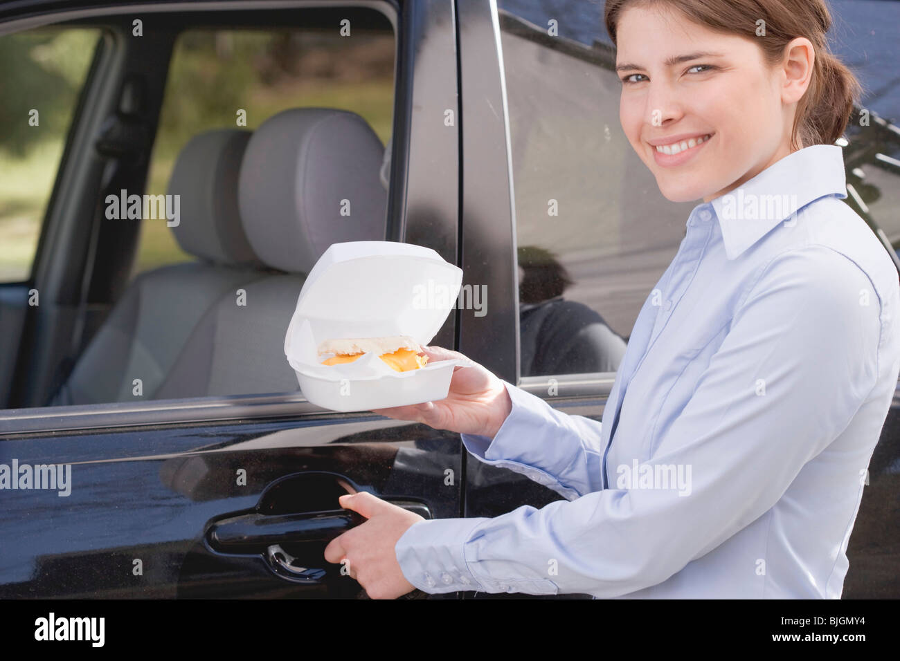 Young woman carrying muffin anglais en boîte en polystyrène pour voiture - Banque D'Images