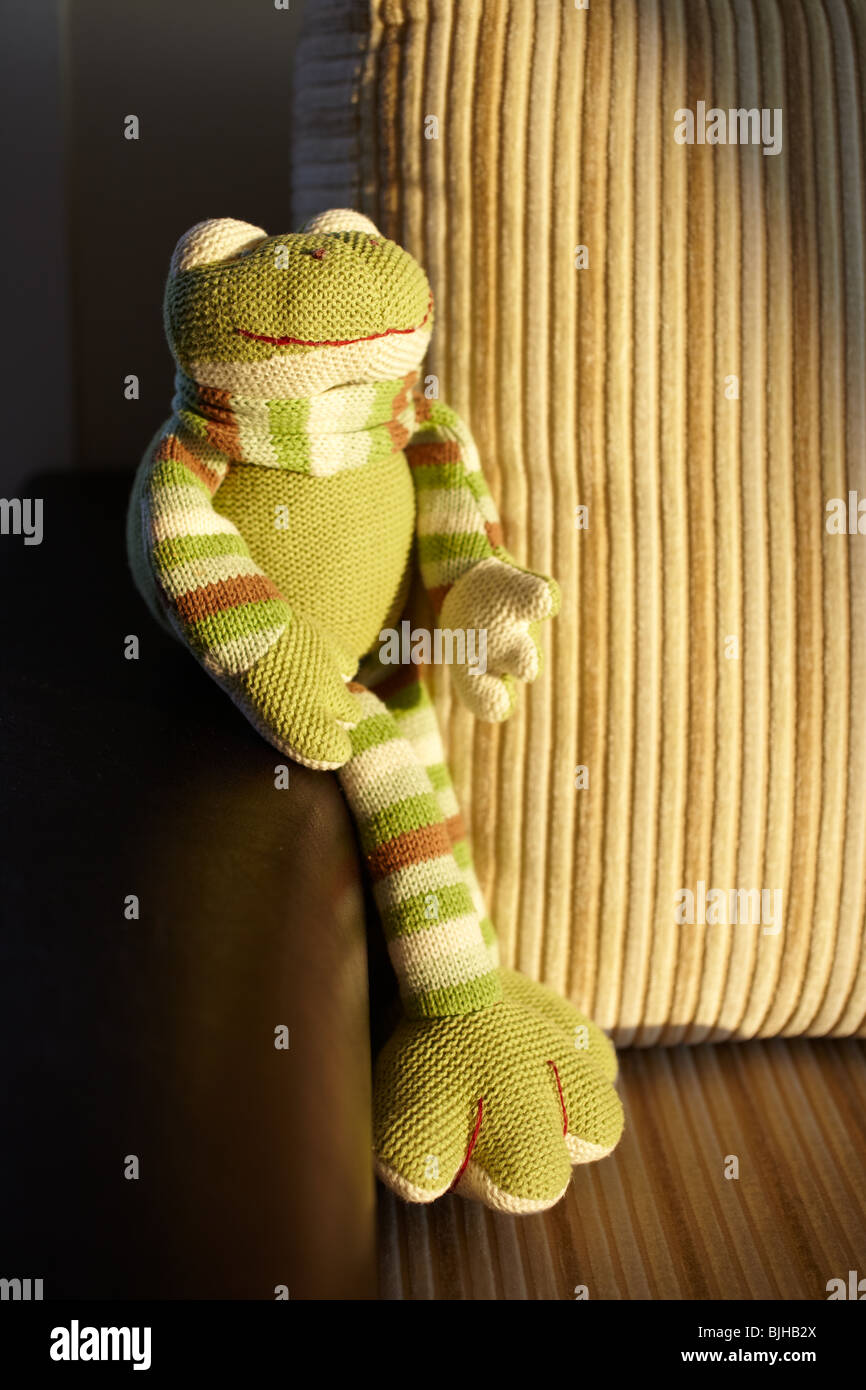 La main verte grenouille jouet tricotés assis dans le dernier rayon de soleil sur un canapé en cuir et velours côtelé marron. Banque D'Images