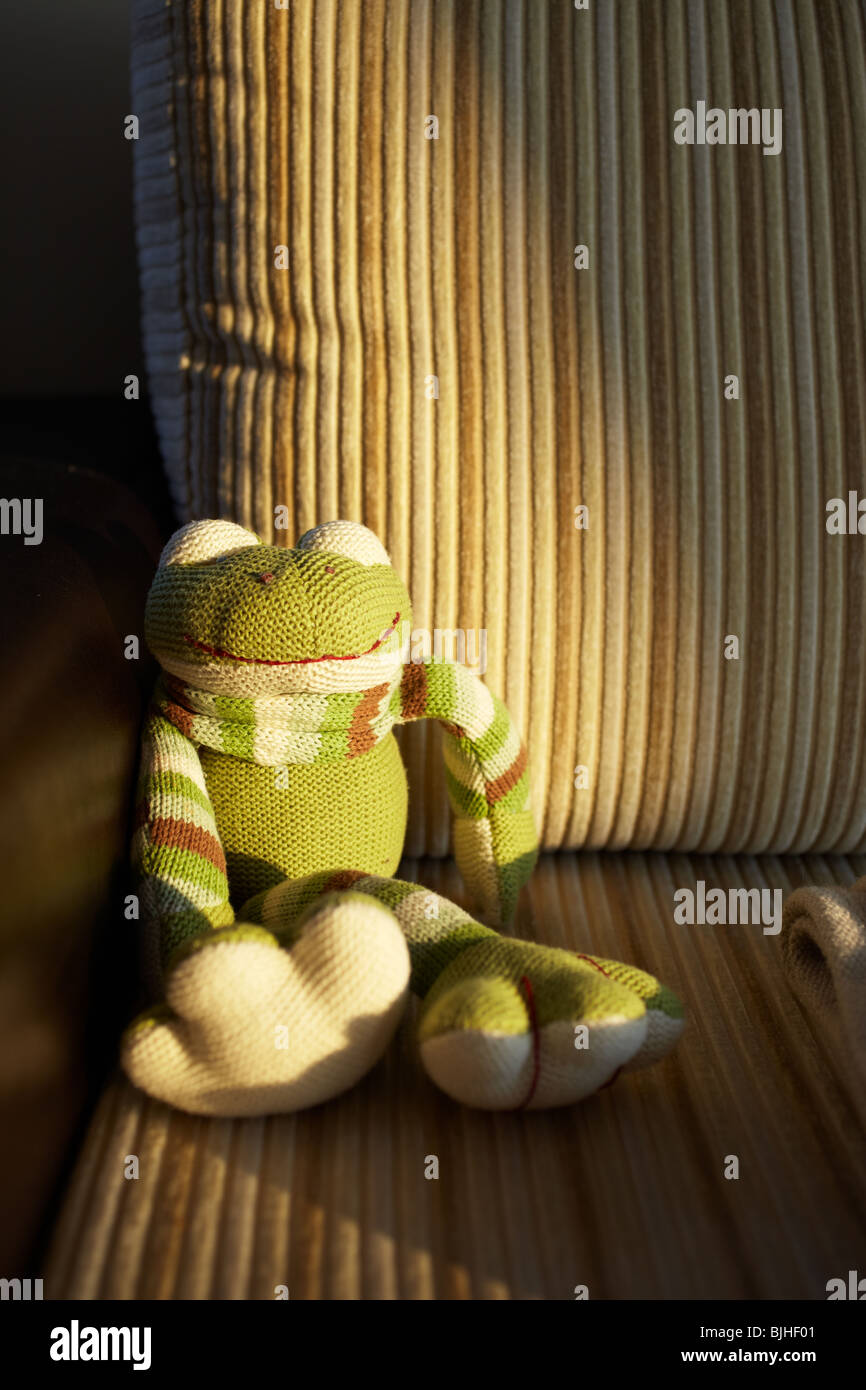 La main verte grenouille jouet tricotés assis dans le dernier rayon de soleil sur un canapé en cuir et velours côtelé marron. Banque D'Images