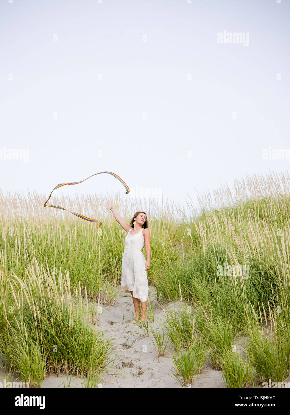 Femme à la plage avec son écharpe souffle loin dans le vent comme elle se  tient sur une dune recouverte de hautes herbes Photo Stock - Alamy
