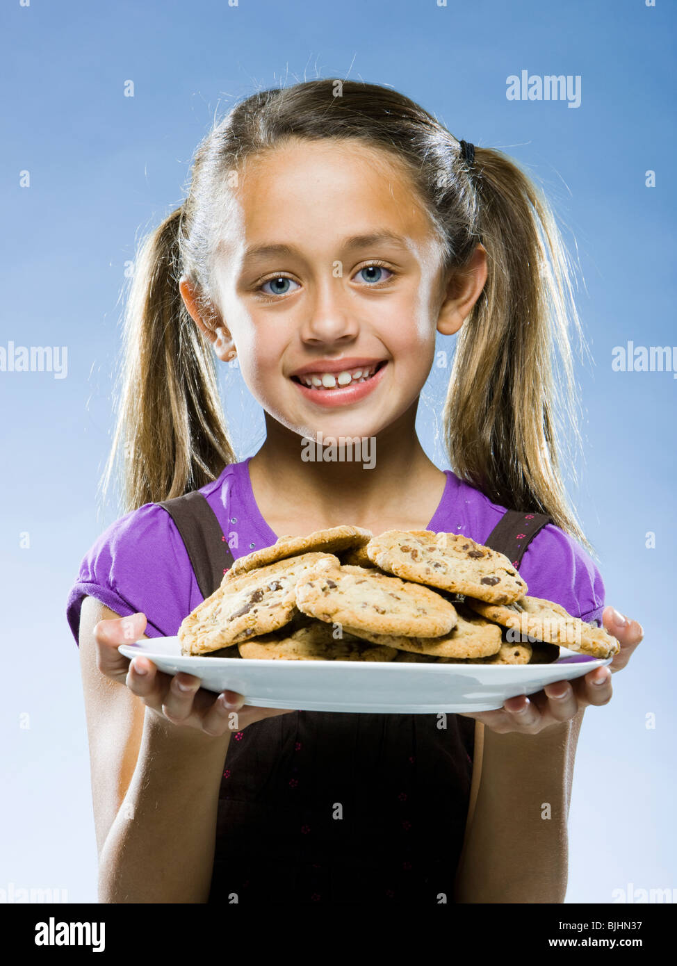 Girl looking at the camera holding a plate of chocolate chip cookies Banque D'Images