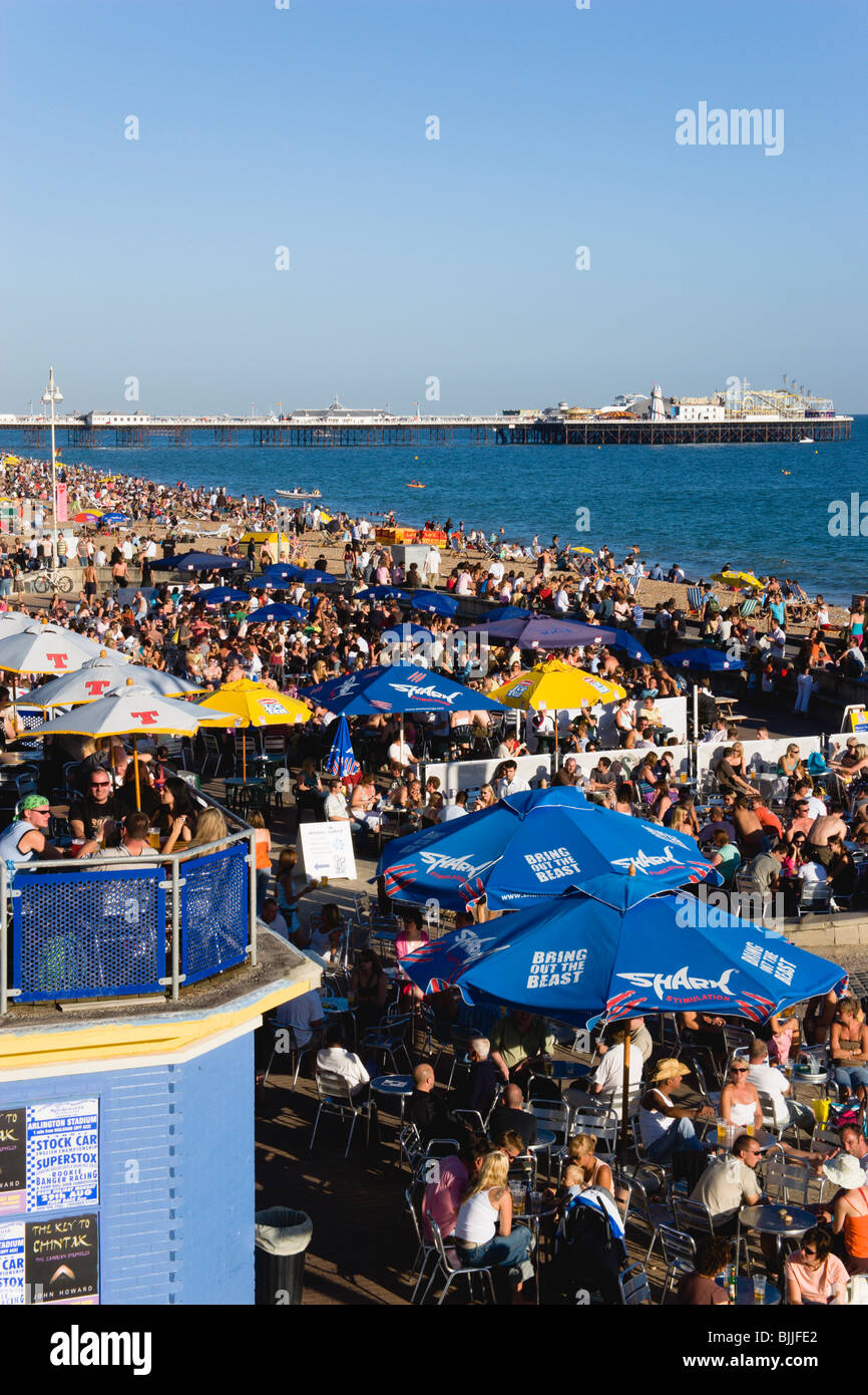 L'Angleterre, l'East Sussex, Brighton, les gens sur la plage et à la promenade du front de mer sur tables de bar avec Pier au-delà Banque D'Images