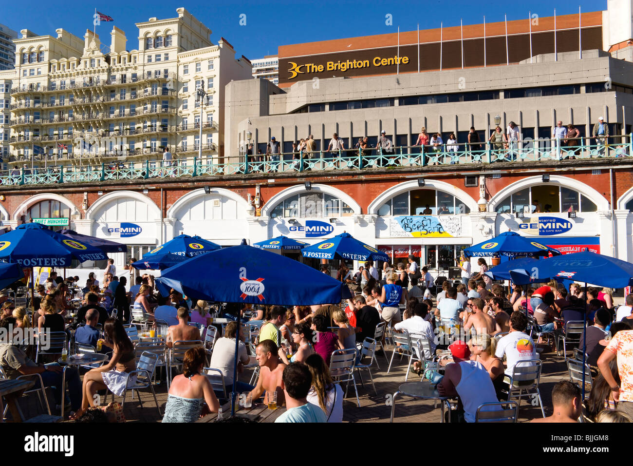 L'Angleterre, l'East Sussex, Brighton, les gens assis à l'ombre de parasols sur des tables sur la promenade à l'extérieur du bar de plage Gemini Banque D'Images