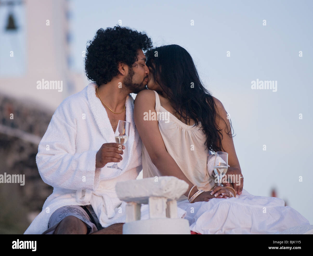 Couple assis en plein air avec des flûtes à champagne et pittoresque et se pelotonnant souriant en arrière-plan Banque D'Images